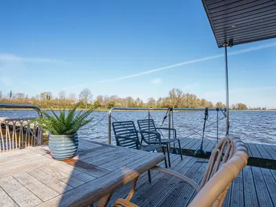 a wooden deck with a table and chairs on the water at Houseboat Campi Uitgeest in Uitgeest