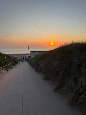 people walking down a sidewalk near the beach at sunset at Elements The Residence Luxe villa en guesthouse in Bergen