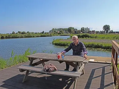 a man sitting at a picnic table next to a river at Apartment by the water in Broek op Langedijk