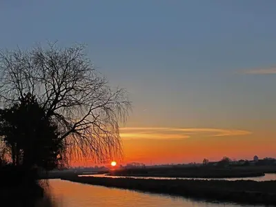 a sunset over a river with a tree in the foreground at Apartment by the water in Broek op Langedijk