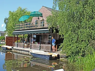 a man standing on a dock next to a house with an umbrella at Apartment by the water in Broek op Langedijk