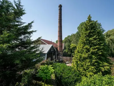 an old factory with a tall chimney and trees at Holiday Home Markermeerlogies by Interhome in Bovenkarspel