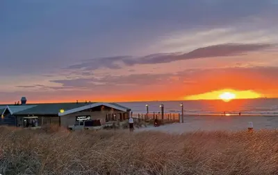 a building on the beach with the sunset in the background at Skip Inn Strandhuisjes in Katwijk aan Zee