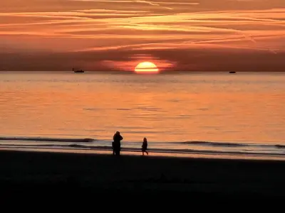 two people walking on the beach at sunset at Skip Inn Strandhuisjes in Katwijk aan Zee