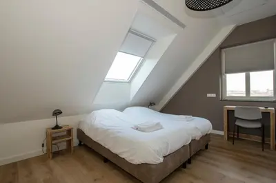 a bedroom with a bed and a desk and two windows at Hotelboerderij Akkerlust in Leidschendam