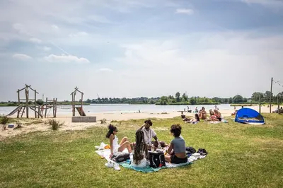 a group of people sitting on the grass at the beach at Cosy Garden Room Riverhouse in Ouderkerk aan de Amstel