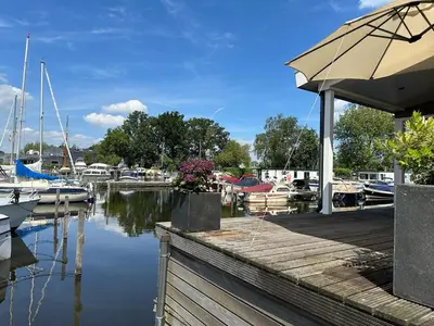 a dock with an umbrella and a marina with boats at Houseboat the Otter incl free boat and supboards in Loosdrecht
