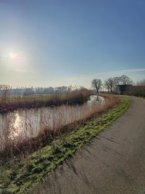 an empty road next to a field with the sun setting at Holiday home in the polder in Abcoude