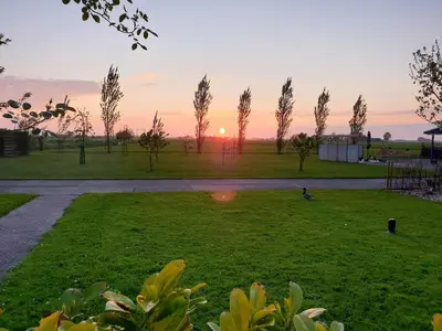a sunset in a park with trees and grass at Complete studio dichtbij Hoorn en Alkmaar in Zuidermeer