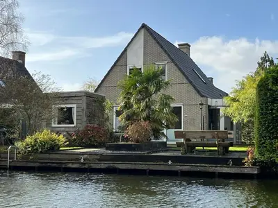 a house with a bench in front of the water at Ferienhaus Aan de Gracht - IJsselmeer in Wervershoof