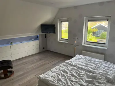 a bedroom with a bed and a tv and two windows at Ferienhaus Aan de Gracht - IJsselmeer in Wervershoof
