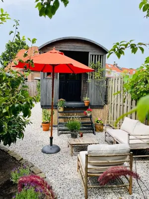 a patio with a red umbrella and a couch and chairs at Tuiny House Noordwijk in Noordwijk