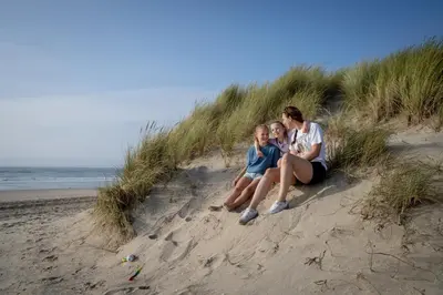 three girls sitting in the sand on the beach at Landal Duynvallei in Schoorl