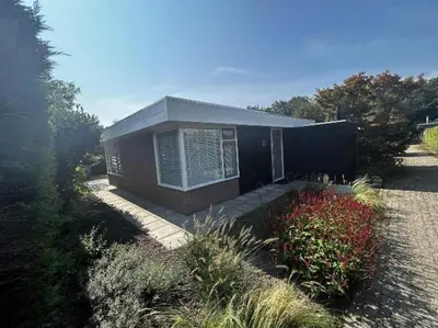 a small house with a black wall and some flowers at Rekerlanden 58 - De Boet in Warmenhuizen