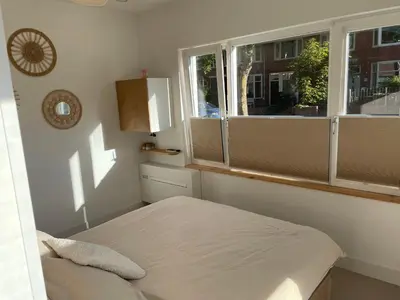 a bedroom with a bed and two windows at Knusse kamer met zonnig terrasje in Zandvoort