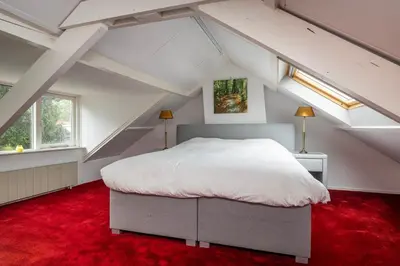 a attic bedroom with a white bed and red carpet at Lovely House in Zeist