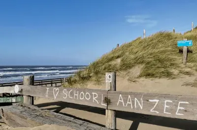 a wooden sign on a beach with the ocean at Huisje aan het einde - 273 in Warmenhuizen