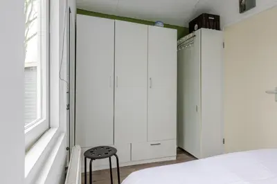 a bedroom with white cabinets and a stool next to a bed at Huisje aan het einde - 273 in Warmenhuizen