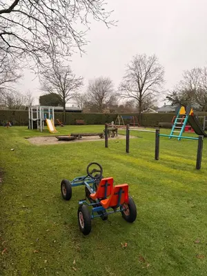 a toy tractor sitting in the grass in a park at Houten familiehuisje Noordwijk met grote tuin in Noordwijk aan Zee