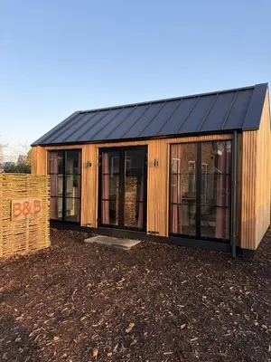 a wooden house with a black roof on a field at B&B Landslake II in Landsmeer