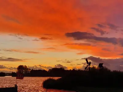 a person and a dog standing in front of a sunset at Holiday Home Chalet op Zee by Interhome in Wervershoof