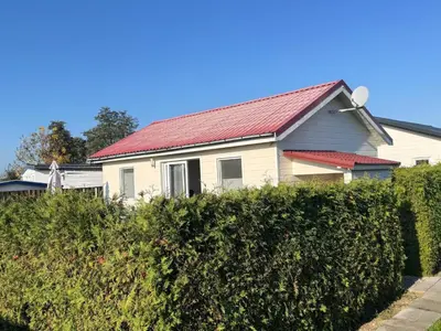 a white house with a red roof behind a hedge at Holiday Home in Wervershoof mit Sonniger Terrasse by Interhome in Wervershoof