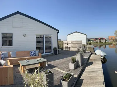 a deck with a couch and a table next to the water at Holiday Home Haus Good Times by Interhome in Wervershoof