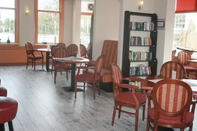 a library with tables and chairs and a book shelf at Zorn Hotel Duinlust in Noordwijk aan Zee