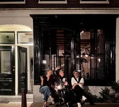 three people sitting on a bench in front of a house at The Design apartment with canal-view in Amsterdam