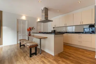 a kitchen with white cabinets and a wooden table at Appartement de Burgemeester - centrum in Castricum