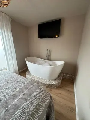 a white tub in a bedroom with a tv on the wall at Romantic jacuzzi suite in the city center in Bodegraven