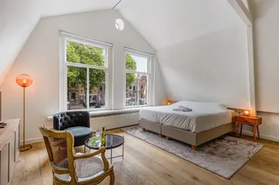 a bedroom with a bed and a chair and a window at Luxury Studio in Utrecht Center - view on canal in Utrecht