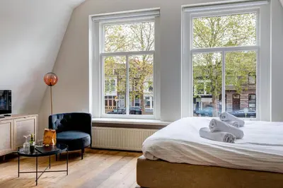 a bedroom with a bed and a chair and windows at Luxury Studio in Utrecht Center - view on canal in Utrecht