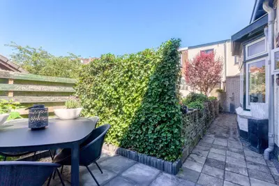 a patio with a table and chairs and a green hedge at Casa Vos Family Home in Zandvoort
