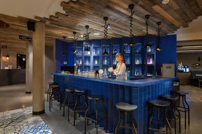 a woman standing at a blue bar with stools at Urban Lodge Hotel in Amsterdam