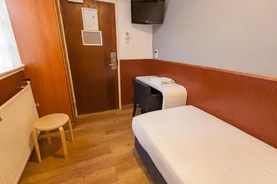 a small room with two beds and a desk and a door at Travel Hotel Amsterdam in Amsterdam