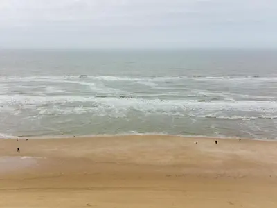 a beach with people walking on the sand and the ocean at Holiday Home De Zeeparel by Interhome in Egmond aan Zee