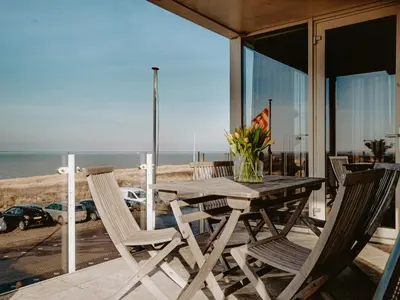 a wooden table and chairs on a deck with the beach at Apartment De Zeeparel by Interhome in Egmond aan Zee