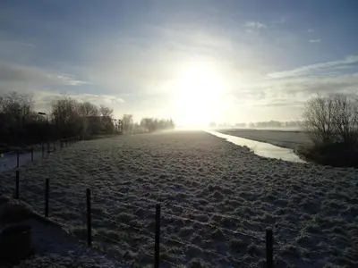 a field covered in snow with the sun in the distance at Aan de Amstel in De Hoef