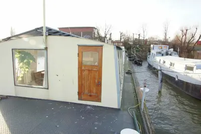 a small house with a door on the side of a canal at The Island Houseboat in Amsterdam