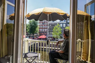 a man sitting on a balcony with an umbrella at The Balcony at Prinsen Canal apartment Amsterdam in Amsterdam