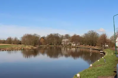 a river in a park with trees and buildings at The Riverside Logies & Restaurant in Maarssen