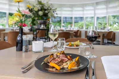 a table with a plate of food and glasses of wine at Fletcher Hotel Restaurant De Witte Raaf in Noordwijk