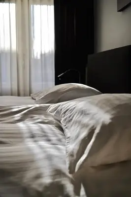 an unmade bed with white sheets and a window at B&B La Festa in Amsterdam