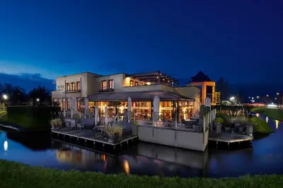 a large building on a river at night at Hotel Babylon Heerhugowaard - Alkmaar in Heerhugowaard