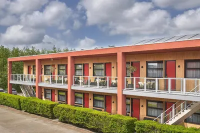 a red building with a balcony with tables and chairs at Hotel Babylon Heerhugowaard - Alkmaar in Heerhugowaard