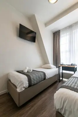 a bedroom with two beds and a tv on the wall at Acostar Hotel in Amsterdam