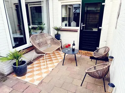 a patio with three chairs and a table with a bottle of wine at Beach House Sea-Esta in Egmond aan Zee