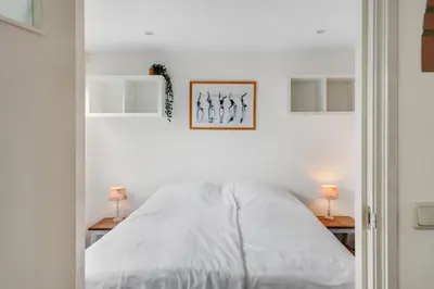 a white bedroom with a bed and two lamps at 't Zwanennest in Egmond aan den Hoef