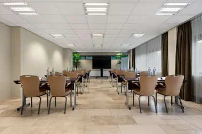 a conference room with tables and chairs and a projection screen at NH Amsterdam Zuid in Amsterdam